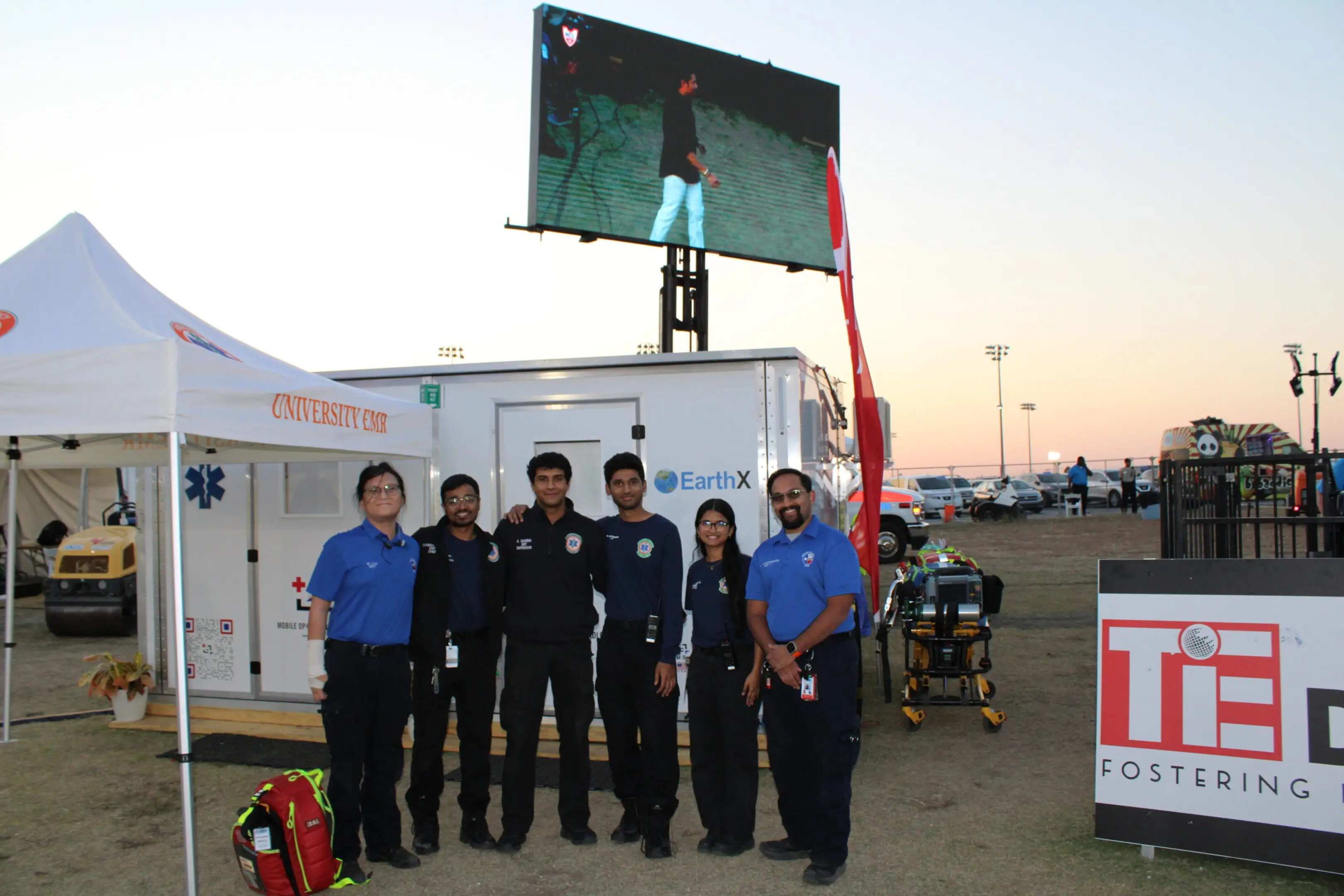 Group of firefighters posing in front of a large screen outdoors at sunset.