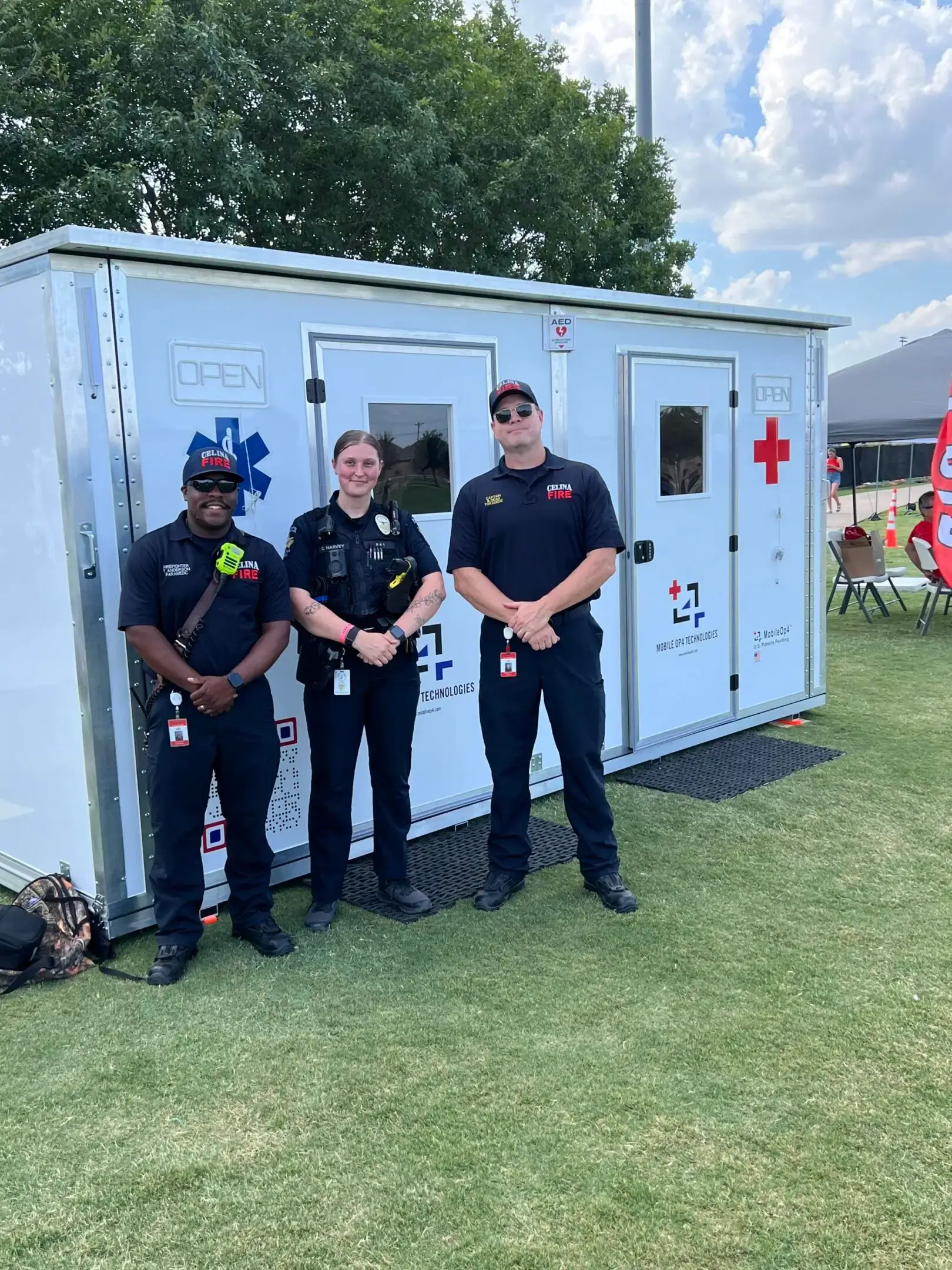 Three emergency responders standing in front of a Red Cross trailer outdoors.